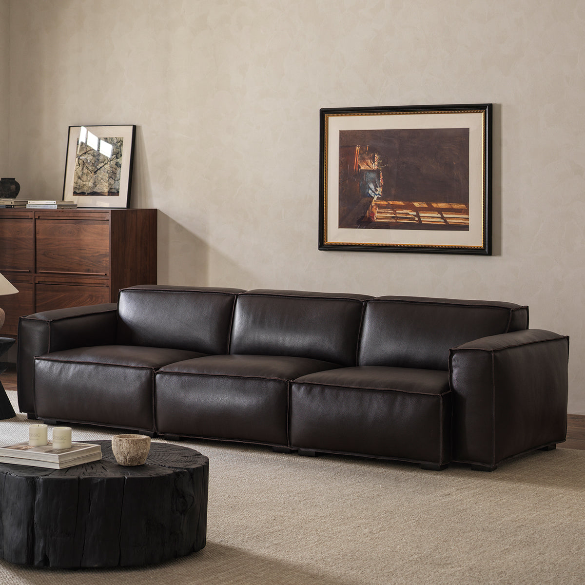 Three-quarter view of black leather sofa in modern living room with charred wood coffee table