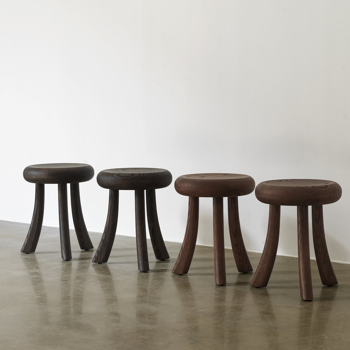 Full lineup view of four solid red oak 3-leg accent stools showcasing different wood finishes