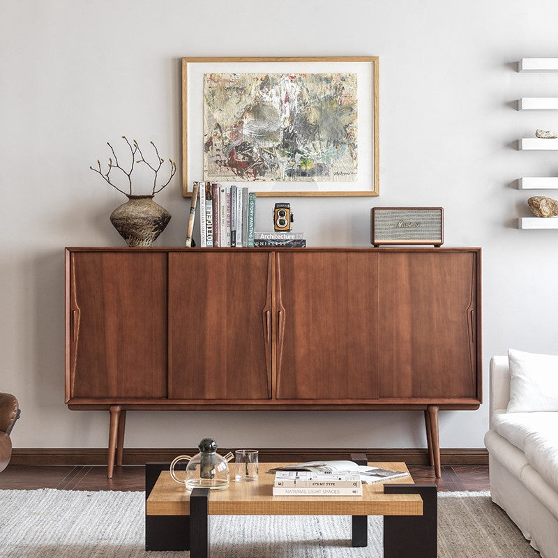 Tall boxwood sideboard in a living room with framed artwork, books and a ceramic vase on top