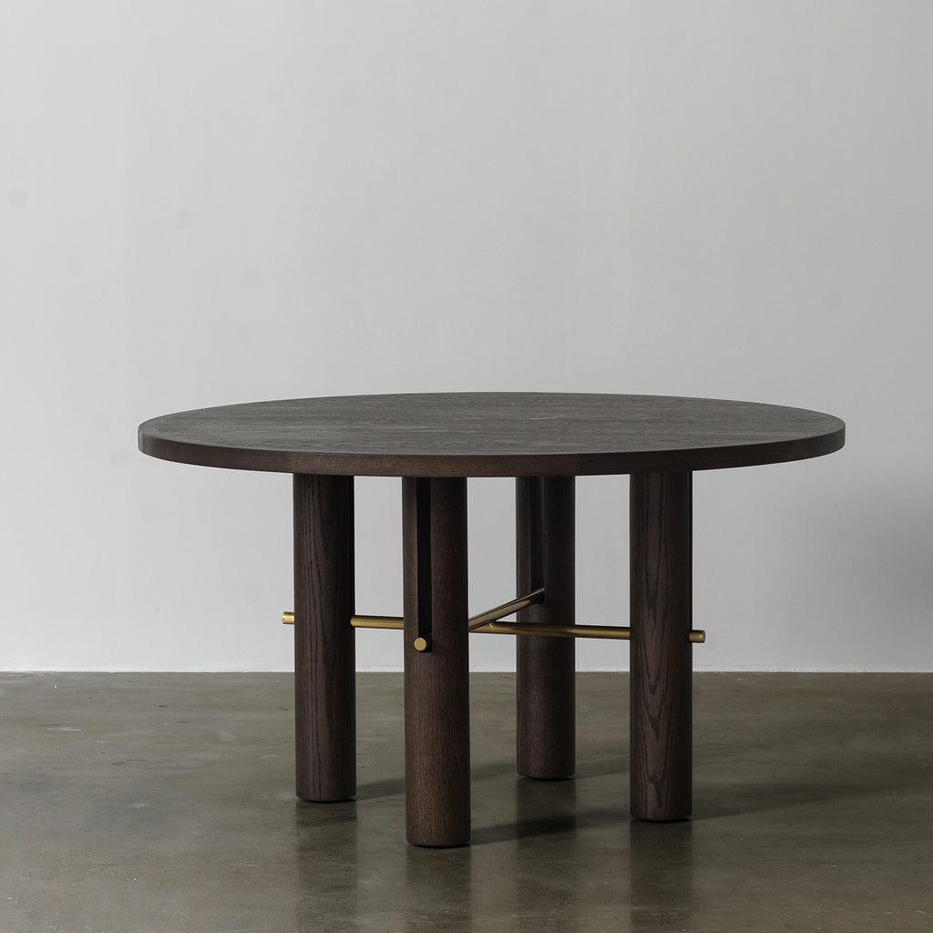 Distressed wood round dining table with cylindrical column legs and brass cross stretcher, front view
