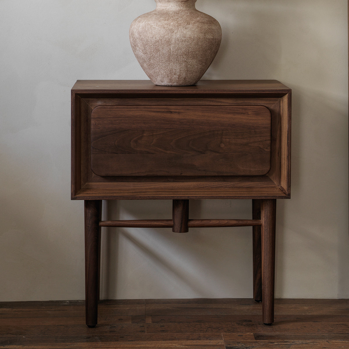 Front view of black walnut nightstand styled with a ceramic vase against an interior wall