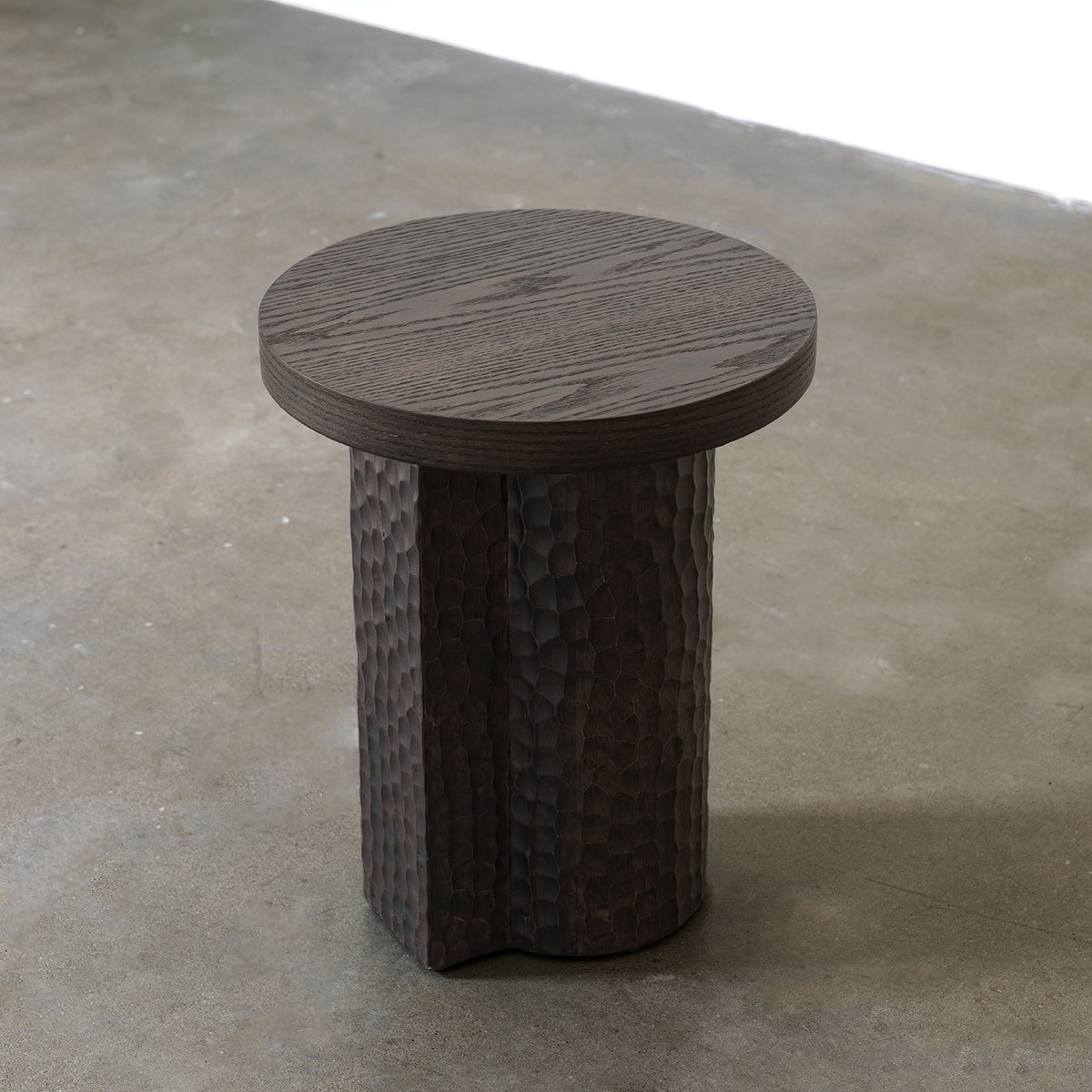 Three-quarter elevated view of round wood side table showing top grain and chiseled column base