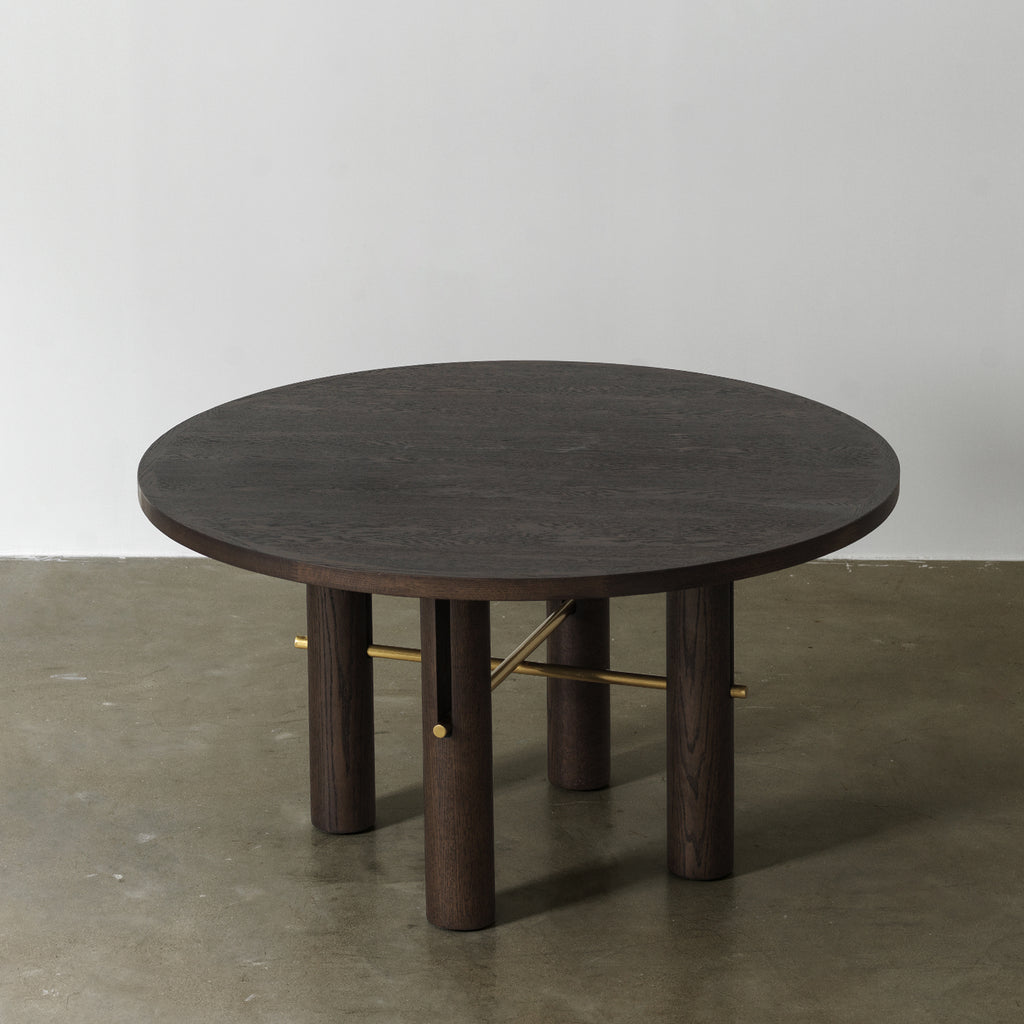 Circular wooden dining table with vintage distressed dark finish and brass accents, three-quarter elevated view