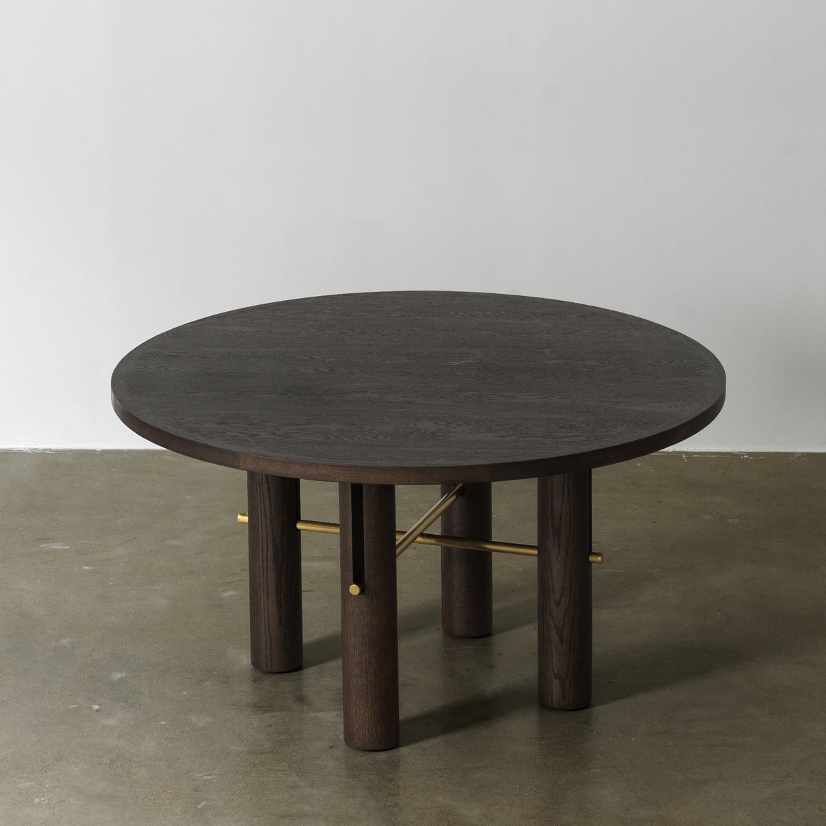 Circular wooden dining table with vintage distressed dark finish and brass accents, three-quarter elevated view
