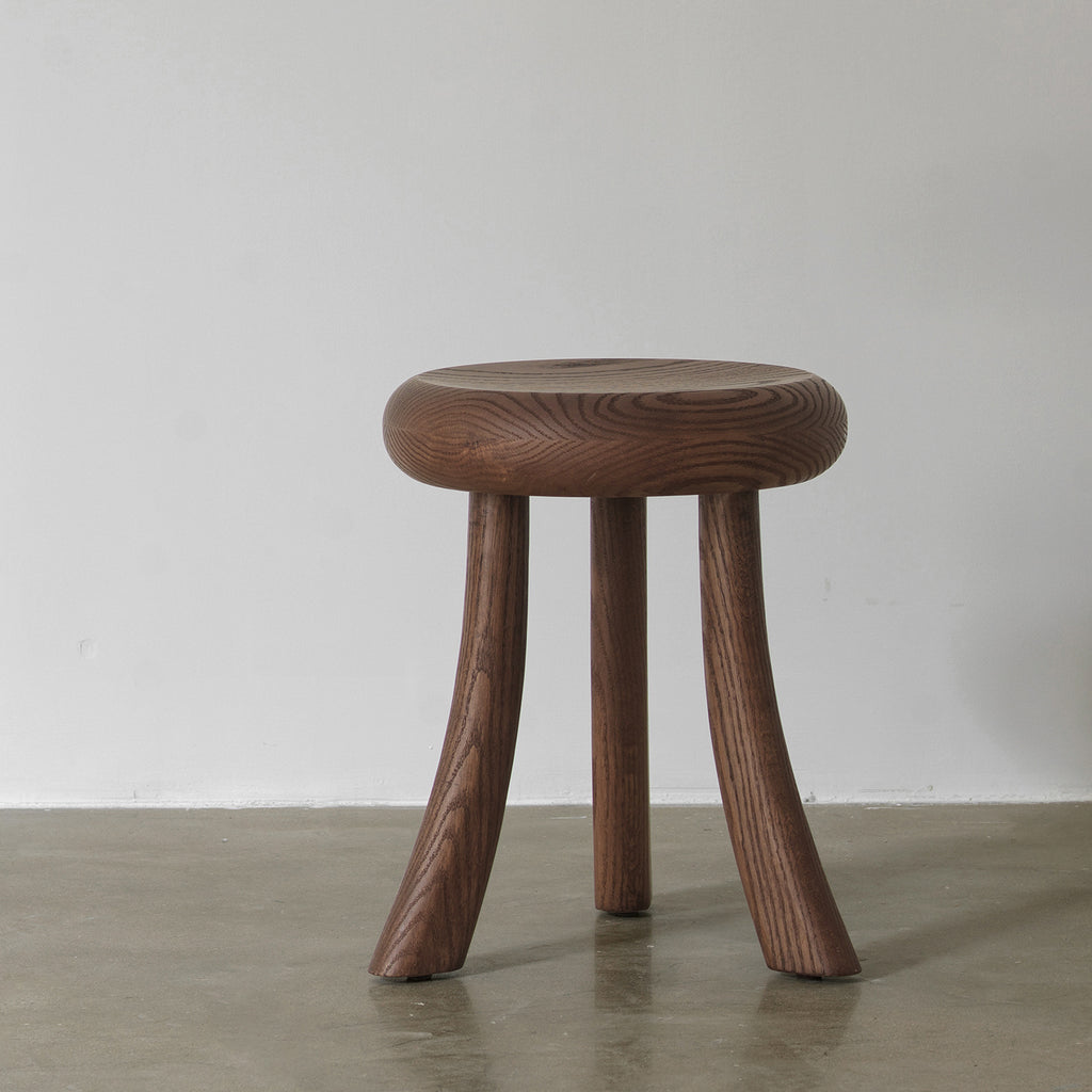Front eye-level view of solid oak 3-legged accent stool and side table against a white wall