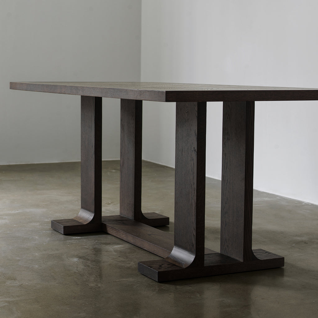 Three-quarter low angle view of vintage wood dining table showing dual-pillar trestle legs and floor stretcher
