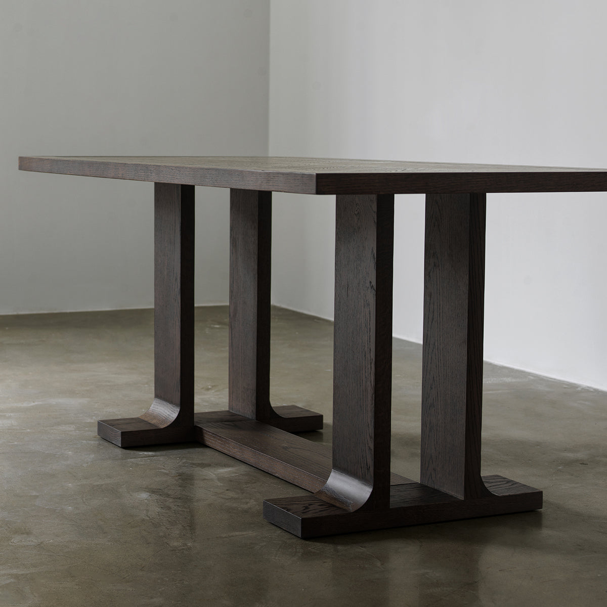 Three-quarter low angle view of vintage wood dining table showing dual-pillar trestle legs and floor stretcher