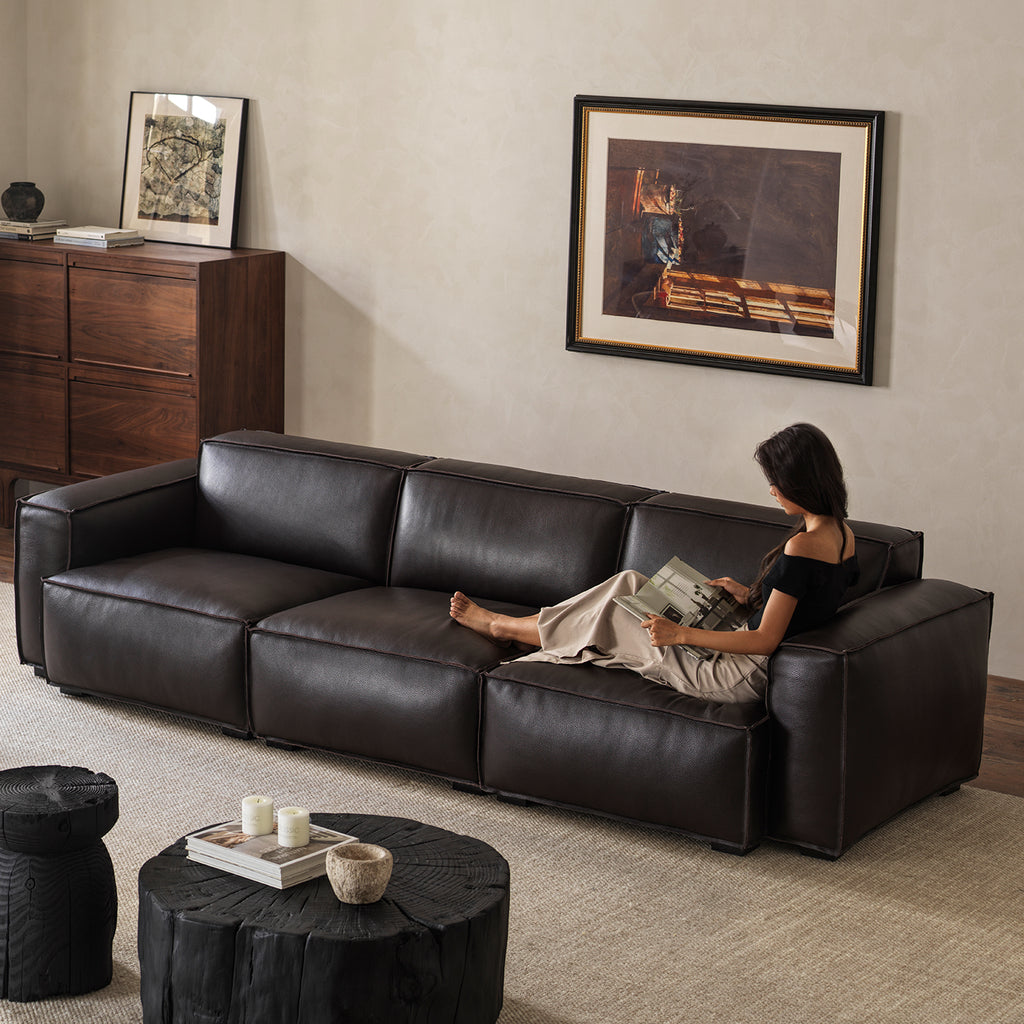 Model relaxing on wide deep-seat black leather sofa in warm minimalist living room setting