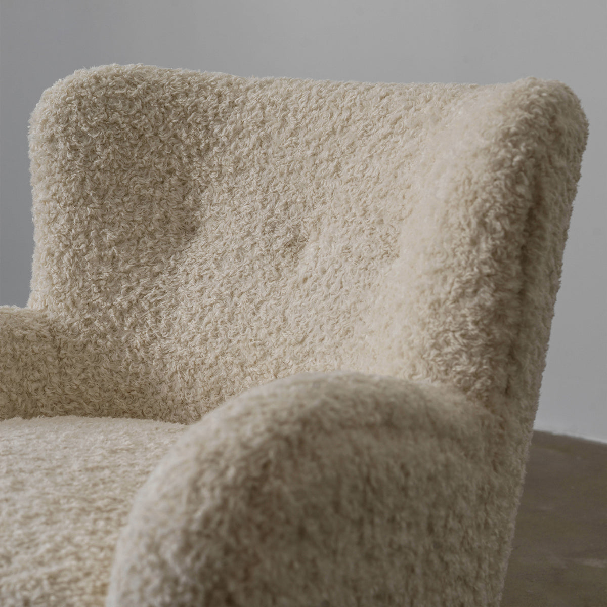 Close-up of Nuantuo chair wingback and rounded arm in cream textured fabric