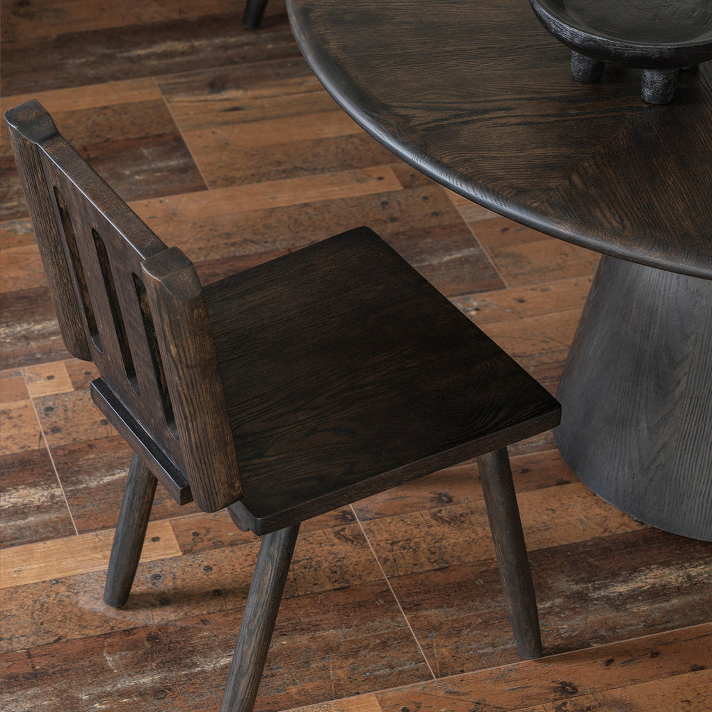 Angled side view of rustic solid wood dining chair next to distressed round dining table