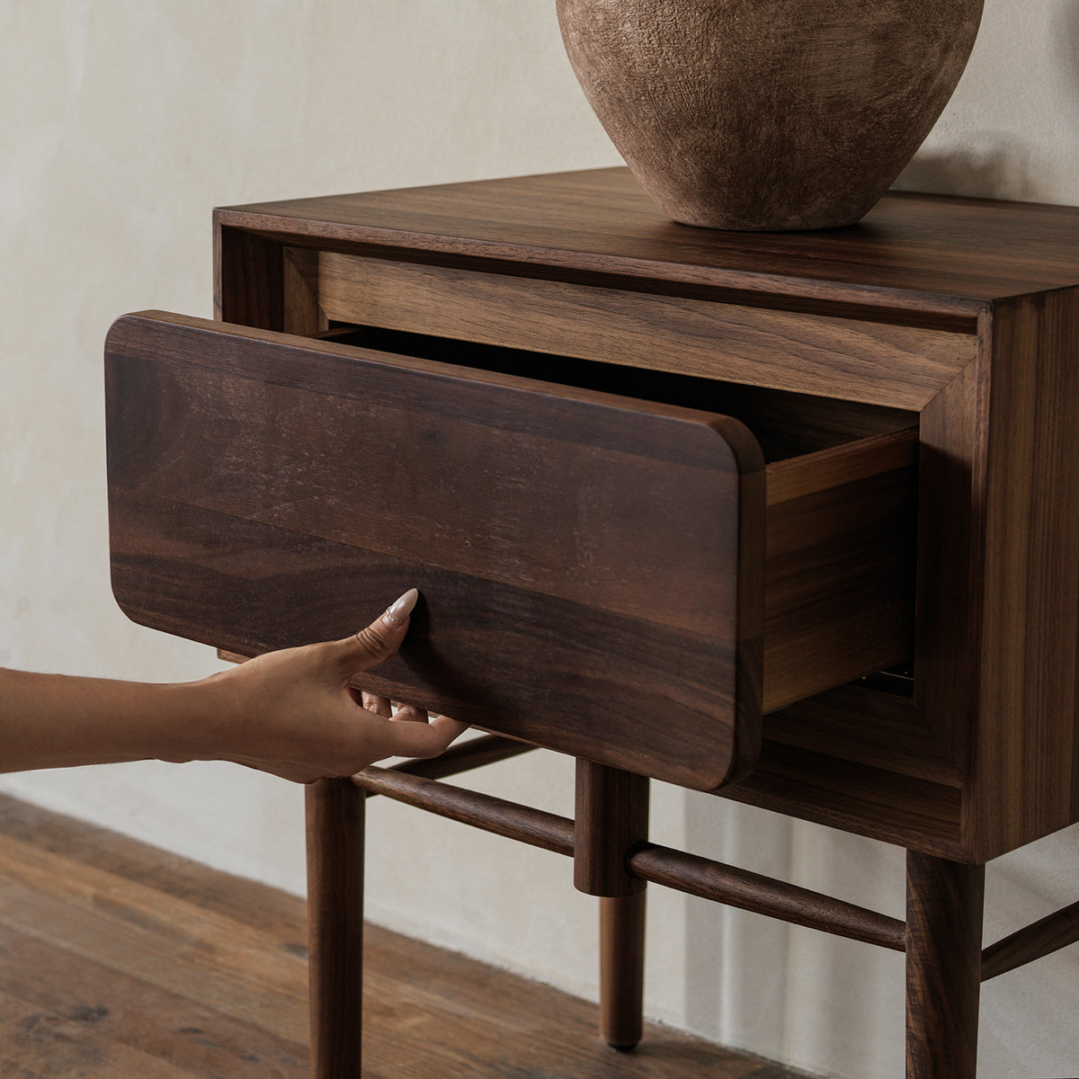 Close-up view of hand opening the handle-free rounded drawer of black walnut nightstand