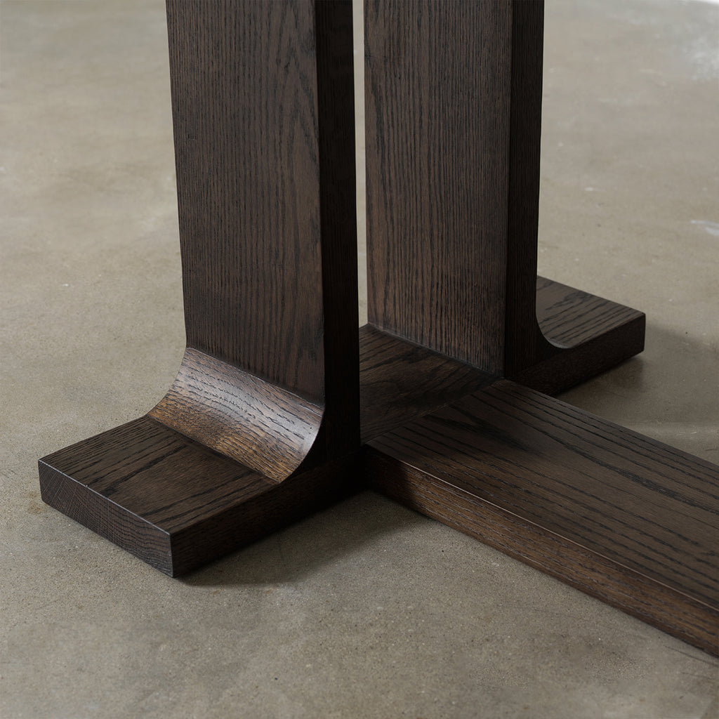 Close-up detail of trestle base foot showing curved wood joint and textured vintage distressed wood finish
