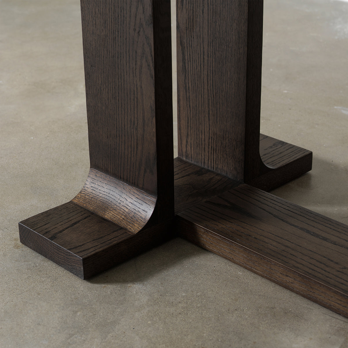 Close-up detail of trestle base foot showing curved wood joint and textured vintage distressed wood finish
