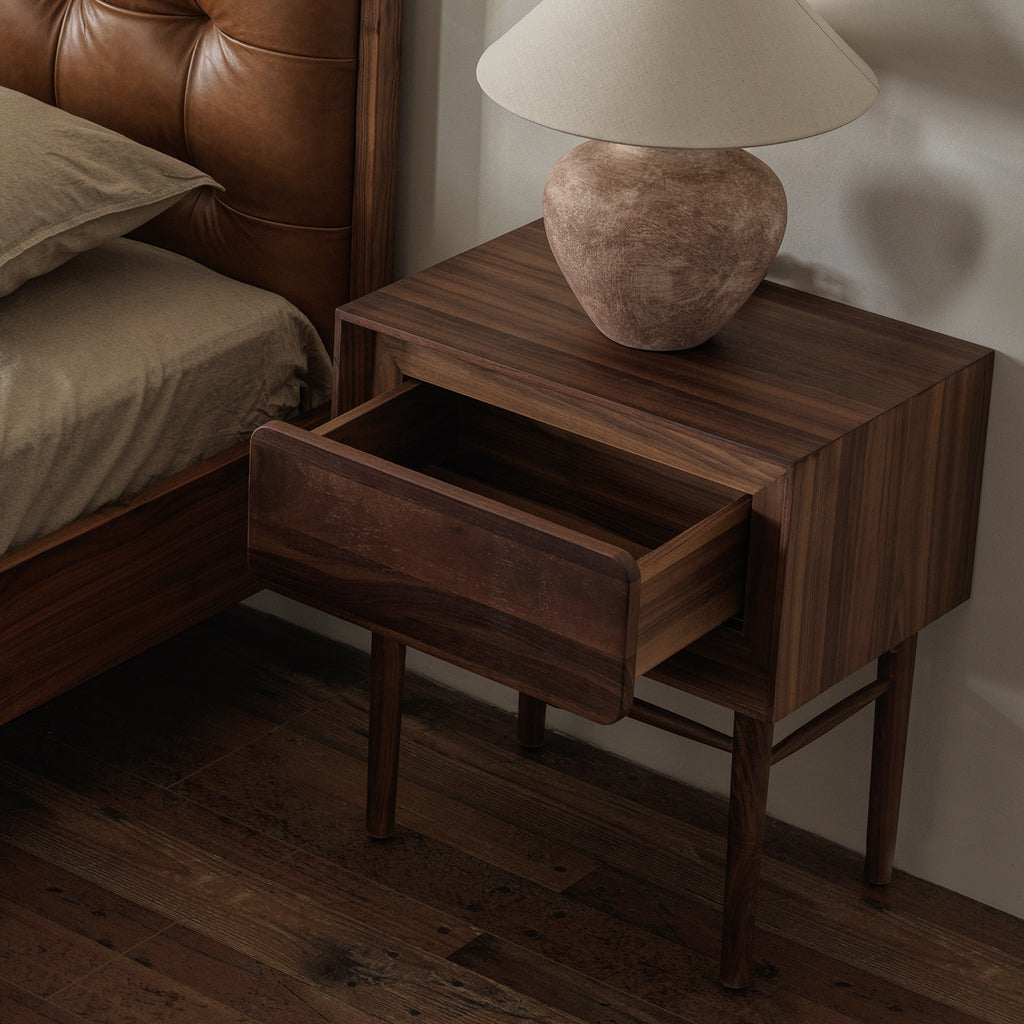 Three-quarter view of black walnut nightstand with drawer pulled open showing interior storage space
