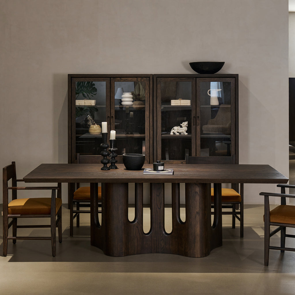 Front view of distressed dark oak dining table paired with chairs in front of glass cabinets in a modern dining room