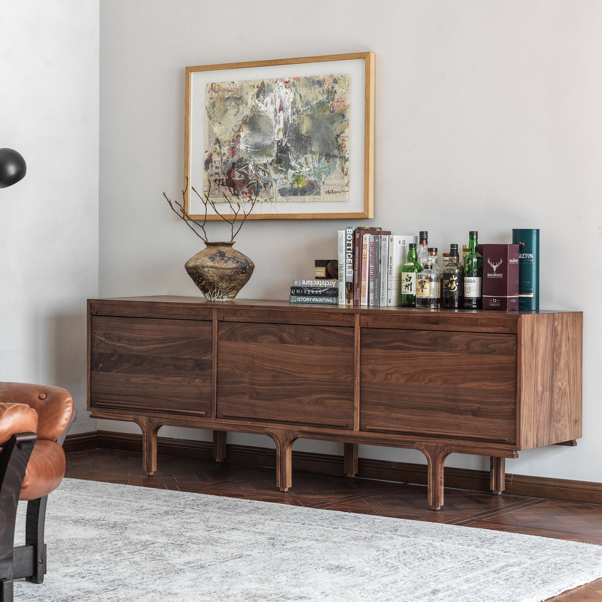 Three-quarter view of an extra-long walnut sideboard next to a brown leather chair